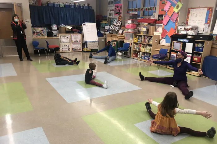 Students and staff do yoga stretches while sitting in a classroom at a Regional Enrichment Center in April.